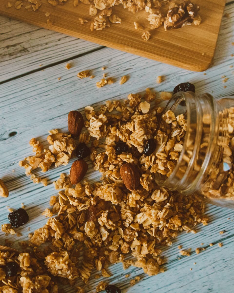 Close-up of homemade granola with almonds and raisins spilling from a jar.
